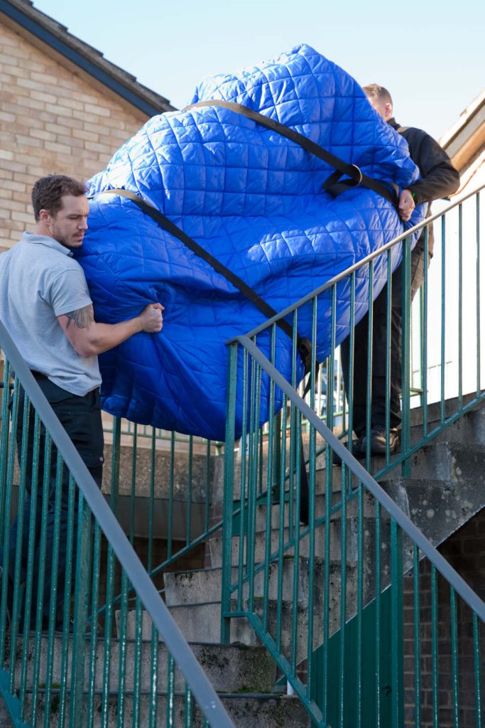 Portrait image of Loads4Less staff member van man lifting sofa down stairs.